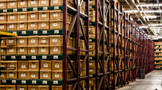Records storage facility with high ceiling; stacks of approximately 12 rows of boxes on shelves