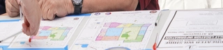A map on a desk, a person's arm on the map. There are two people at this desk